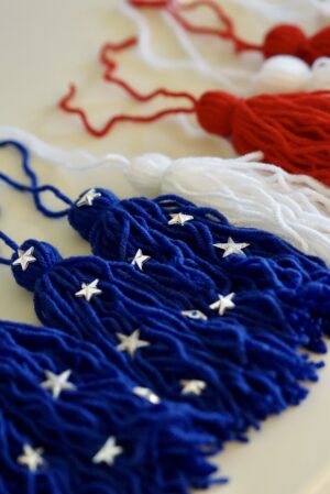 Picture of tassels to be used in making a red, white, and blue American flag themed tassel garland.  There are 3 blue tassels with silver stars decorating them, followed by alternating white and red tassels. 